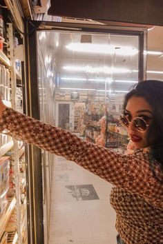 a woman standing in front of a store window holding out her hand to the camera