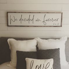 a bed topped with pillows next to a wooden sign that says we decided on forever