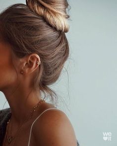 a woman with her hair in a high bun, looking down at the camera and wearing earrings