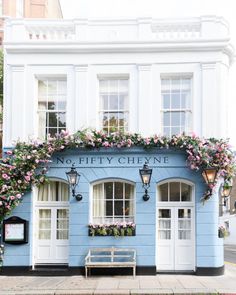 a blue building with pink flowers on the windows and door, next to a bench