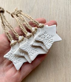 a hand holding three white ceramic ornaments with twine on each ornament hanging from strings