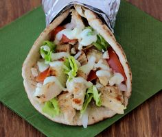 a wrap filled with chicken and lettuce on top of a green napkin next to a wooden table