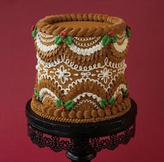 a decorated cake sitting on top of a black stand against a red background with white and green decorations