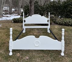 a white bed sitting on top of a grass covered field next to trees and bushes