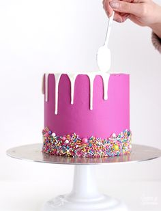 a person is cutting into a pink cake with white icing and sprinkles