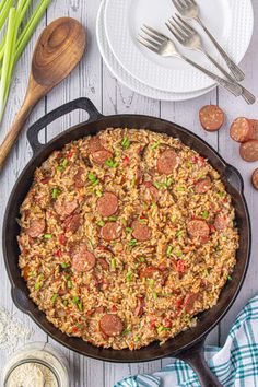 a skillet filled with rice and pepperoni on top of a wooden table next to green onions