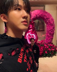 a woman standing in front of a pink heart shaped object with her hand on her shoulder