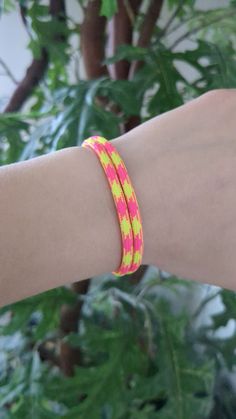 a woman's arm with a pink and yellow bracelet on top of her wrist