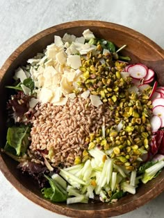 a wooden bowl filled with lots of different types of vegetables and grains next to sliced radishes