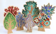 four wooden trees with colorful mosaic designs on them, all in different shapes and sizes