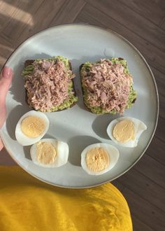 a person holding a plate with eggs and tuna on it, which are cut in half