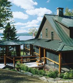 a large house sitting on top of a lush green hillside next to a lake and forest