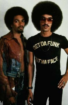 two men standing next to each other in front of a white wall wearing afro wigs