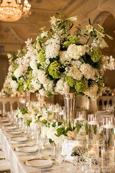 a long table is set with white and green flowers in tall vases on it