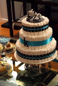 a three tiered wedding cake with blue ribbon and shoes on top, sitting on a glass table