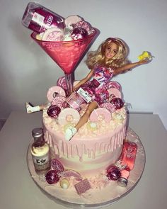 a barbie doll sitting on top of a pink cake next to a cocktail glass and bottle