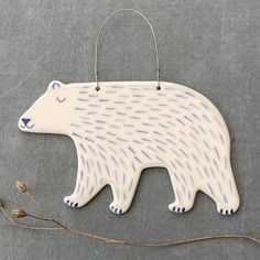 a ceramic bear ornament hanging from a twig on a gray tablecloth