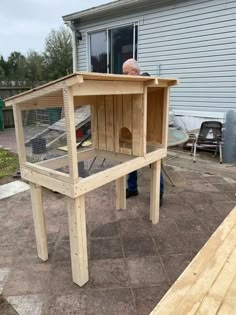 a man standing next to a chicken coop on top of a wooden deck in front of a house