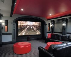 a home theater with black leather couches and red pillows on the seats, along with a large screen