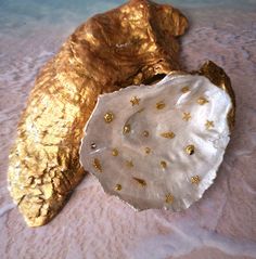 two pieces of gold and white are on a pink surface, one is shaped like a shell