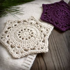 two crocheted coasters sitting on top of a wooden table next to a pine tree