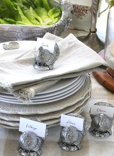 a table topped with plates covered in silver turkey napkin holders and place cards on top of each plate