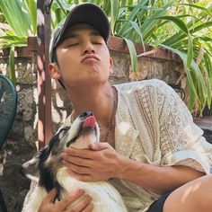 a man holding a dog in his lap while sitting on the ground next to some plants