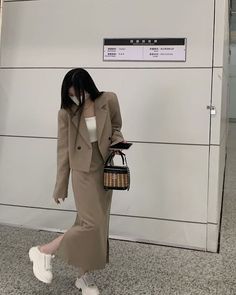 a woman in a beige coat and white shoes is walking through an airport with her handbag