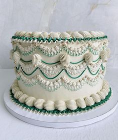 a three layer white cake with green trimmings and shells on the bottom tier