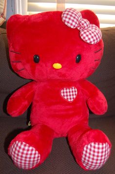 a red hello kitty stuffed animal with a heart on it's chest sitting on a couch