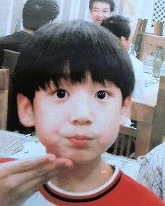 a young boy holding his hand up to his face while standing in front of other people