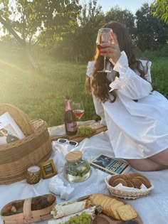 a woman sitting at a picnic table with food and wine in front of her face