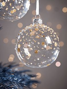 two glass ornaments hanging from a christmas tree with gold and silver decorations on it's branches