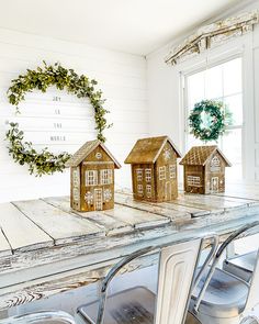 three wooden houses sitting on top of a white table next to a wreath and chairs