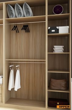 an open wooden closet with clothes hanging on the shelves and folded towels in front of it