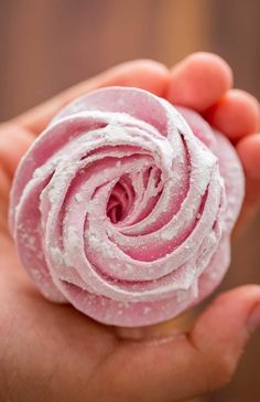 a hand holding a pink donut with white frosting