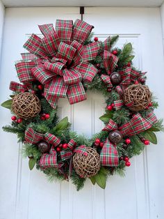 a christmas wreath with red and green plaid bow hanging on a white front door,