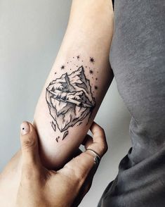 a woman's arm with a mountain tattoo on it and stars in the sky