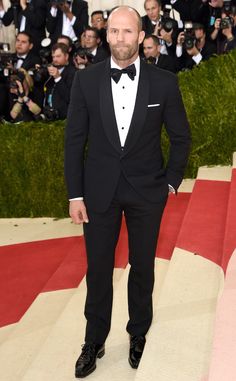 a man in a tuxedo and bow tie stands on the red carpet at an event