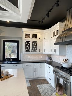 a young child standing in the middle of a kitchen with white cabinets and black counter tops