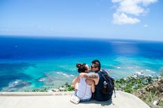 a man and woman sitting on top of a cliff overlooking the ocean