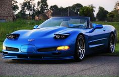 a blue sports car is parked on the side of the road in front of some grass