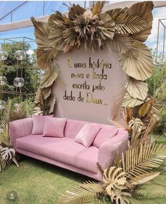 a pink couch sitting on top of a lush green field next to a wall covered in leaves