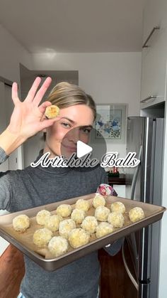 a woman holding a tray full of doughnuts in front of her face and hands