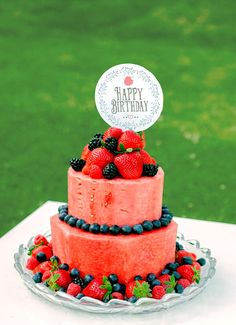 a three tiered cake with berries and blueberries on top is decorated with a happy birthday sign