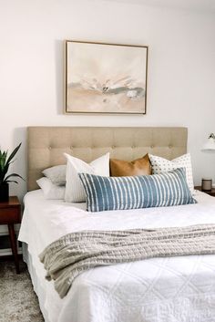 a bed with white linens and pillows in a small room next to a painting on the wall