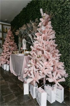 pink christmas trees are lined up in front of a wall with greenery on it