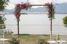 two white chairs with pink flowers on them are set up for an outdoor ceremony by the water