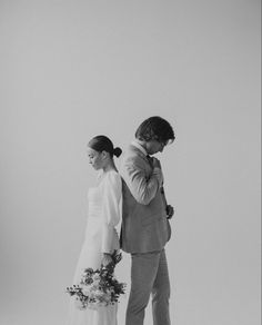 a man and woman standing next to each other in front of a white wall holding flowers