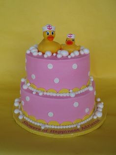 two rubber ducks sitting on top of a pink and yellow cake with white polka dots